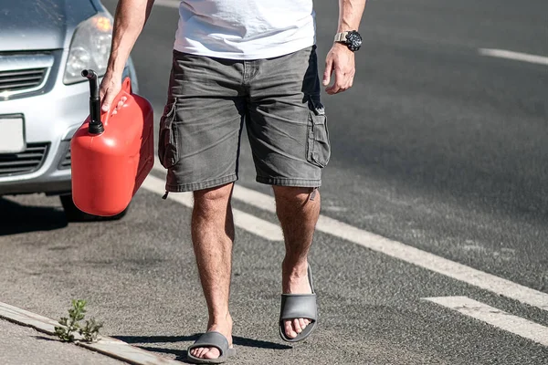 A red canister on the asphalt near the car. The car ran out of gas and stalled. A young man hoping for help on the road from other drivers. Royalty Free Stock Photos