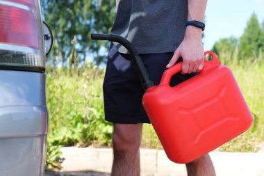 Arabanın yanındaki asfaltta kırmızı bir kutu var. Arabanın benzini bitti ve stop etti. Diğer şoförlerden yardım bekleyen genç bir adam..