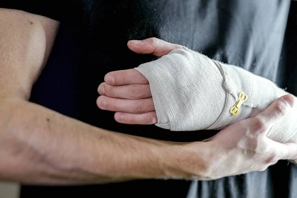 Adam yaralı eli destekliyor. Birincil bakım, el elastik bir bandajla sıkıca sabitlenmiş.. — Stok fotoğraf