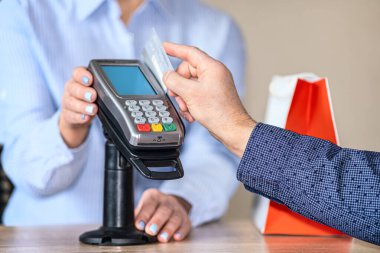 Bir adam mobil terminal kullanarak online alışveriş yapıyor. Terminal okuyucudan plastik bir kart geçirir.