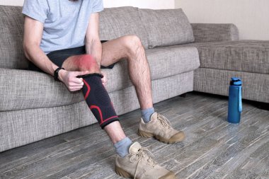 Adam yaralı dizine baskı bandajı koyuyor. Spor etkinlikleri için hazırlanan hassas nokta kırmızıyla vurgulandı.