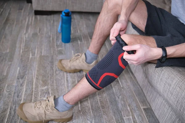 Ten chlap dává na zraněné koleno tlakový obvaz. Příprava na sportovní aktivity, bolavé místo je zvýrazněno červeně. — Stock fotografie