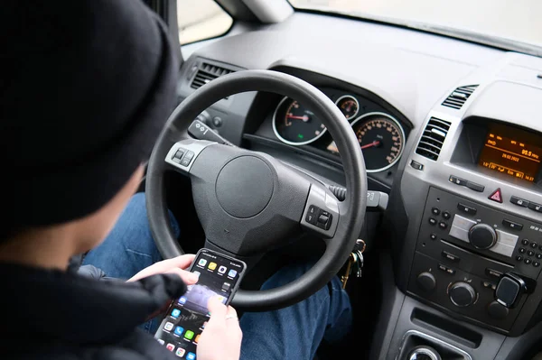 De bestuurder houdt het stuur niet vast met zijn handen. Hij kijkt in zijn smartphone. Stockfoto