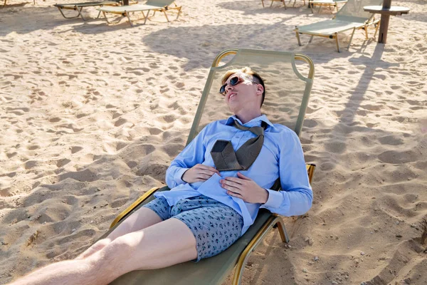 Giovane uomo d'affari stanco si trova su una chaise longue in camicia con cravatta e boxer. Riposa in mare, riavvia. Diminuzione — Foto Stock