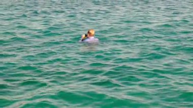 Gömlekli, kravatlı ve çoraplı komik bir adam sudan çıkar ve güneşli bir günde denize yüzer. Yavaş çekim, 4k