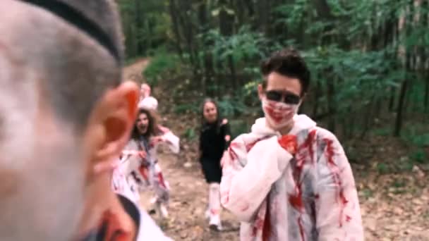 Halloween. Un grupo de personas vestidas de zombis, con ropa blanca manchada de sangre, caminan por el bosque durante el día. cámara lenta, 4k. — Vídeos de Stock