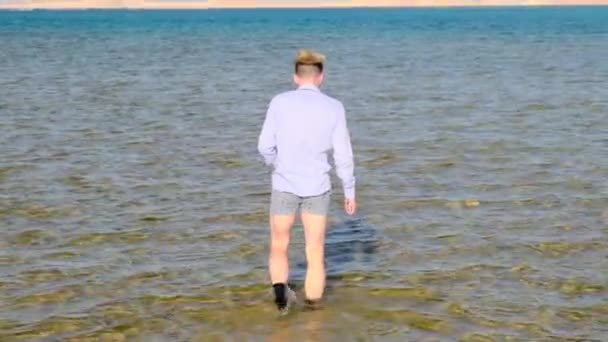 Muž v košili, šortkách a ponožkách jde do moře a obrací se zády. Zpomalený pohyb, 4k — Stock video