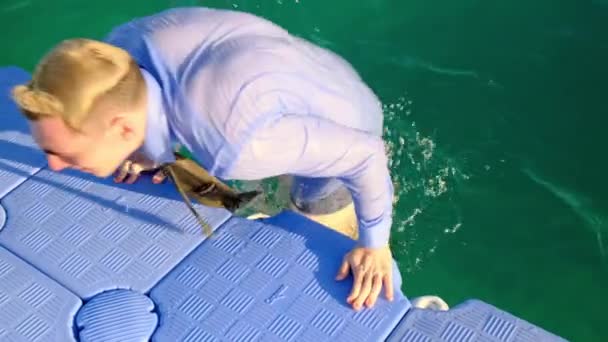 Un jeune homme drôle émerge de l'eau et s'assoit sur la jetée en chemise, cravate et short. Mouvement lent, 4k — Video