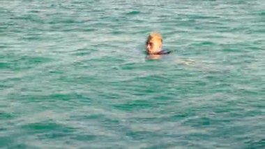 Gömlekli ve kravatlı komik bir adam güneşli bir günde denizde yüzer. 4k