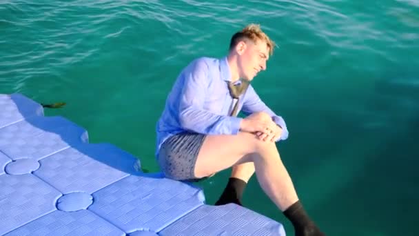셔츠를 입고 양말 과 반바지를 입은 웃긴 남자 가 부두에 앉아 있다가 바다로 떨어진다. 슬로우 모션 , 4k — 비디오