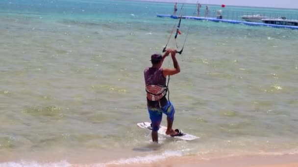 Kite surfen jongeman. Gelooide jongeman gooit plank in het water, staat erop, rijdt langs golven, touwen van parachute in zijn handen. Zomer sport. Egypte, Sharm El Sheikh, 22 april 2021 — Stockvideo