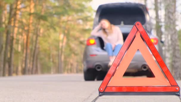 Попередження про червоний трикутник. Сумна молода жінка сидить у багажнику сірого автомобіля з блимаючим аварійним світлом вздовж дороги, чекаючи на допомогу. Вона підстрибує вгору і біжить на дорогу, щоб зловити прохідну машину. Повільний рух, 4k — стокове відео