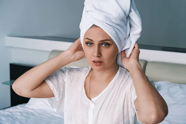 Portret van een jonge vrouw met een handdoek op haar hoofd na een douche. Blauwe ogen meisje kijkt in de camera het aanpassen van de handdoek op haar hoofd. Ze zit op het dak in een wit gewaad.. Rechtenvrije Stockafbeeldingen