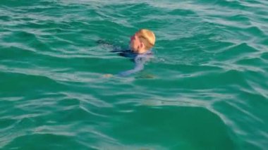 Gömlekli, kravatlı ve çoraplı komik bir adam güneşli bir günde denizde yüzer. Yavaş çekim, 4k