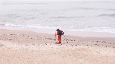 Adam kumda metal dedektörle yürüyor. Elektronik metal dedektörü ve bir atlatma haber. Bir adam, turistlerin denizde ve plajda kaybettiği lüksü arıyor. Deniz kenarı, köpüklü dalgalar. 4k, ağır çekim.