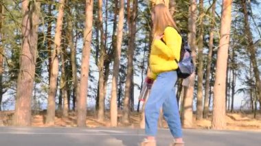 Otostop konsepti. Sarı ceketli, elinde termosla sırt çantalı genç bir turist çam koruluğu boyunca yol boyunca yürüyor. Seçici odaklanma. Yavaş çekim, 4k