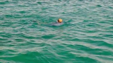 Gömlekli, kravatlı ve çoraplı komik bir adam güneşli bir günde denizde yüzer. Yavaş çekim, 4k