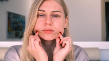 Yüz geliştirme. Çift çene problemi. Çekici sarışın bir kadının portresi parmaklarıyla yüz masajı yapıyor. Kişisel bakım. Yaşla ilgili değişikliklerle savaşmak. 4k, ağır çekim.