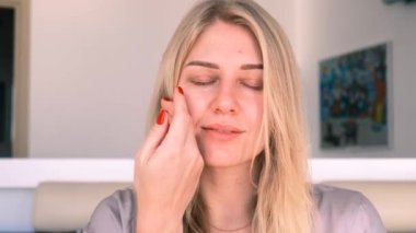 30 yıl içinde doğal güzellik ve öz bakım. Genç ve güzel sarışın bir kadının portresi nazikçe yüzüne dokunuyor, kameraya bakıyor. 4k, ağır çekim.