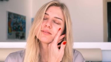 30 yıl içinde doğal güzellik ve öz bakım. Genç ve güzel sarışın bir kadının portresi nazikçe yüzüne dokunuyor, kameraya bakıyor. 4k, ağır çekim.