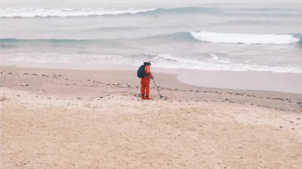 Metal dedektörlü bir adam plaj boyunca kırmızı bir elbiseyle yürüyor. Ağır çekim, 4k, ağır çekim. — Stok video