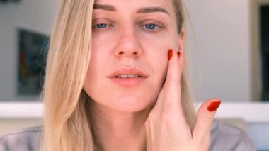 30 yıl içinde doğal güzellik ve öz bakım. Genç ve güzel sarışın bir kadının portresi nazikçe yüzüne dokunuyor, kameraya bakıyor. 4k, ağır çekim.