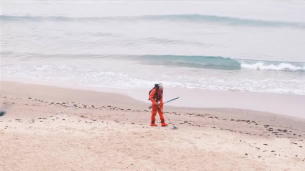 Un hombre con un detector de metales en la playa. El hombre está buscando joyas en la playa. Pasa un sensor especial a través de la arena, buscando cosas metálicas o metales no ferrosos. cámara lenta, 4k — Vídeos de Stock