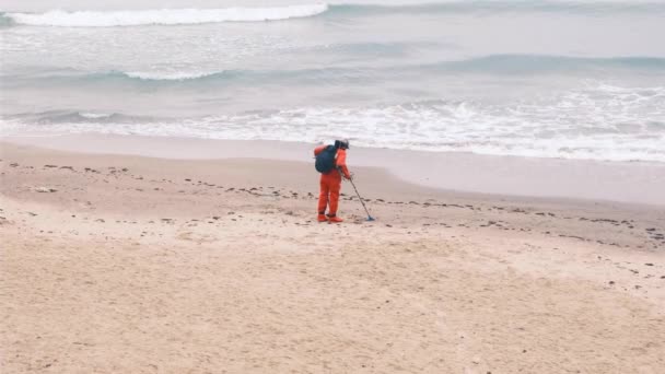 Metal dedektörlü bir adam plaj boyunca kırmızı bir elbiseyle yürüyor. Yavaş çekim, 4k. — Stok video