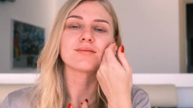 30 yıl içinde doğal güzellik ve öz bakım. Genç ve güzel sarışın bir kadının portresi nazikçe yüzüne dokunuyor, kameraya bakıyor. 4k, ağır çekim.