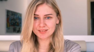 Kendine güvenen genç, mavi gözlü, makyajsız sarışın kadın kameraya bakıyor. Bir kızın sabah portresi. Yavaş çekim, 4k
