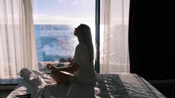 精神衛生だ。海とパノラマの窓を背景に瞑想の若い女性の側のビュー。スローモーション4k — ストック動画