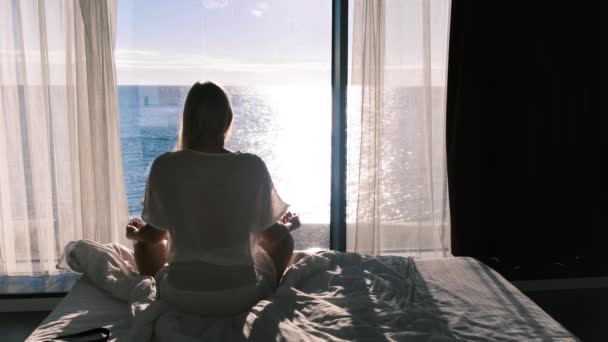 Mentális egészség. Hátsó kilátás egy meditáló fiatal nő hátterében a tenger és a panoráma ablak. Lassú mozgás, 4k — Stock videók