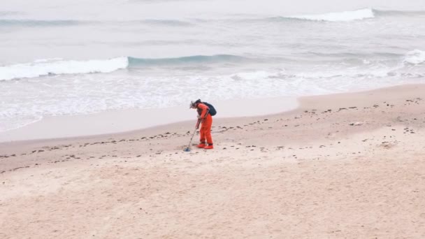 L'uomo cammina con un metal detector nella sabbia. metal detector elettronico e uno scoop. Un uomo è alla ricerca dei lussi persi dai turisti in acqua e sulla spiaggia. Mare, onde schiumose. 4k, rallentatore. — Video Stock