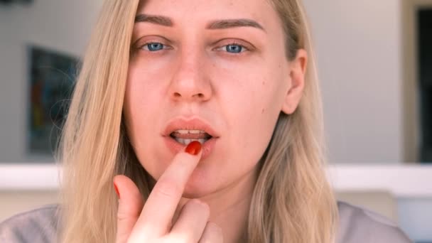 Portrait d'une jeune fille appliquant un baume hydratant sur ses lèvres. Belle blonde aux yeux bleus prend soin de son visage, regardant dans la caméra, au ralenti, 4k — Video