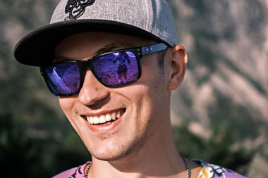 Çekici, güler yüzlü, güneş gözlüklü bir adam, kameraya bakar..