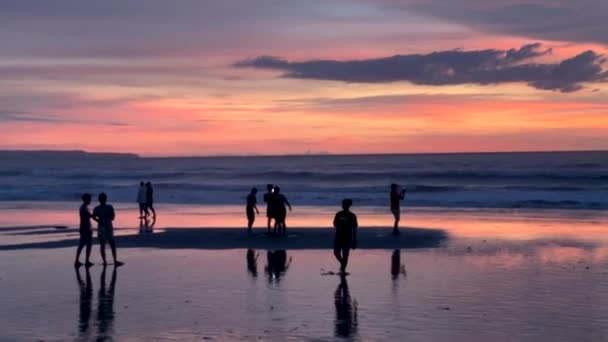 Silhouetten van mensen bij zonsondergang tegen de achtergrond van de oceaan op het strand. Een schilderachtige kleurrijke zonsondergang op de Indische Oceaan. Bali, Indonesië, 1 april 2022 — Stockvideo