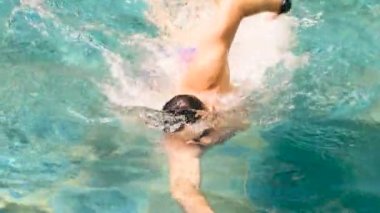 Yüzücü, zümrüt renkli bir havuzda antrenman yapıyor. Yüzme gözlüğü takan genç sporcu antrenman sırasında emekleyerek yüzüyor ve yarışmalara hazırlanıyor. Profesyonel sporlar. Yavaş çekim, 4k