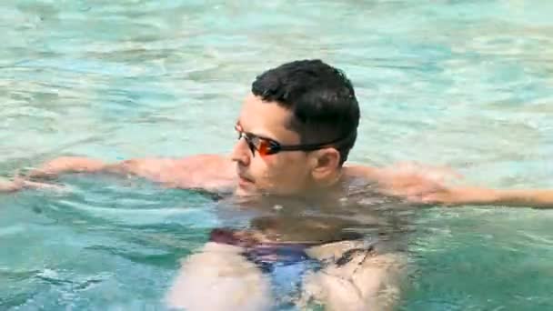 Nadador. Jovem atlético morena homem vestindo óculos de natação na piscina. Bandeira Panorama. Estilo de vida saudável. Atleta sério contra fundo de água azul-turquesa. Exercícios cardiovasculares de esportes e fitness. — Vídeo de Stock