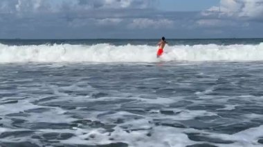 Endonezya 'nın Bali açıklarında öfkeli Hint Okyanusu' nda yüzen atletik adam kameraya beyaz köpüklü büyük sörf dalgaları yaklaşıyor. Aşırı boş zaman..