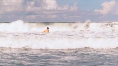 Endonezya 'nın Bali açıklarında öfkeli Hint Okyanusu' nda yüzen atletik adam kameraya beyaz köpüklü büyük sörf dalgaları yaklaşıyor. Aşırı boş zaman..