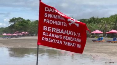 Tehlike, yüzmek yasaktır, Endonezya 'daki Bali adasının kumlu sahilinde kafatası olan kırmızı uyarı bayrağı. Kuvvetli bir rüzgarda dalgalanan bayrak kumlu plajın arka planında ve bulutlu gökyüzünde.