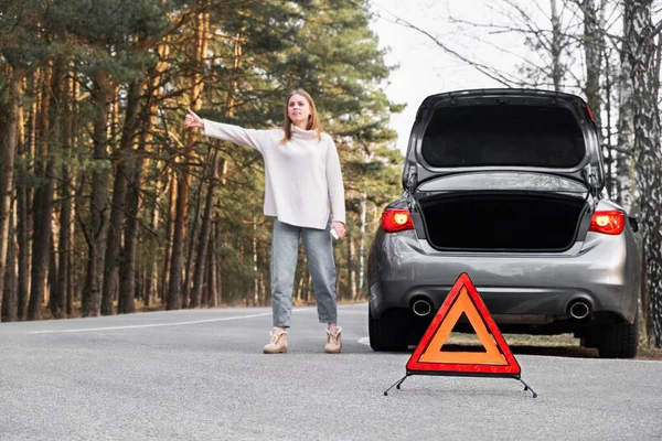 Red emergency triangle with blurred car and woman calling car mechanic in the background. Accident and broken car on the road.