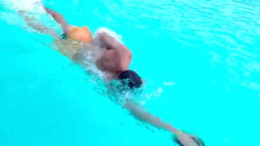 Yüzücü. Profesyonel yüzücü yarışma için havuzda hazırlanıyor. Yüzme gözlükleri ve dalga kürekleri takan genç atletik adam havuz boyunca özgürce yüzüyor.
