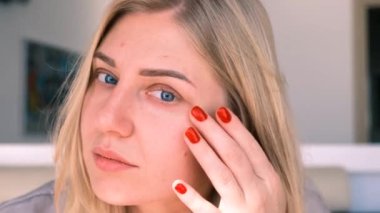 Mavi gözlü, genç ve çekici bir sarışının portresi. Kameraya bakıyor. Temiz, parlak yüzünde kırışıklıklar arıyor. Yaşlanma sorunları, cilt sağlığı ve tazeliği