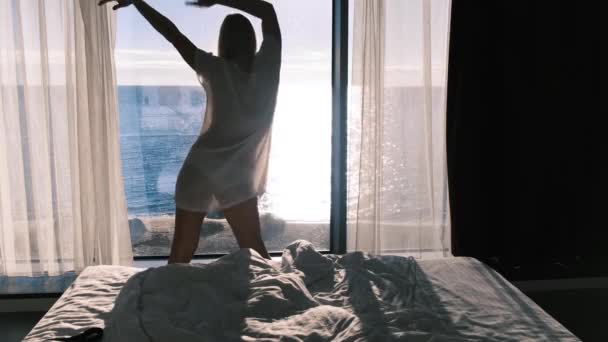 晴れた日に海を見下ろすパノラマの窓を背景に 透明なバスローブを着た女性が踊ります 幸福感 喜びと満足感 バックビュー — ストック動画