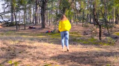 Gezinti. Turist bir kızın portresi, güneşli bir baharda sarı bir ceketle ormanın içinde temiz havanın tadını çıkarıyor. Huzur, sükunet, zevk, 4k, yavaş çekim