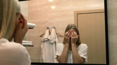 Yaşlanma. Gevşek deri. Banyodaki aynaya bakarken yüz gerdirme egzersizi yapan genç bir kadın. Facebook binası. Modern bakım, yüz kaslarının gevşemesi. Yüz gerdirme, estetik ameliyat