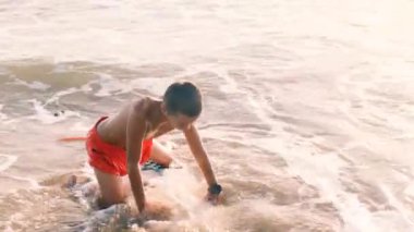 Sörf tahtasına mayo giyen Asyalı genç Portret gün batımında kıyıya çıktı. Dalga çocuğu kıyıya sürükledi. Bali, Endonezya, 28 Haziran 2022