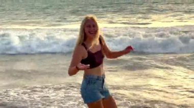 Dişlerinde diş teli olan genç mutlu sarışın kız, Endonezya 'nın Bali adasında, Jimbaran plajında Hint Okyanusu' nun turkuaz dalgalarına karşı okyanusta yakalanan yengeci taşıyor..