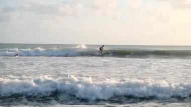 Olağanüstü bir spor. Okyanusta sörfçüler. Akşam sörfü. Birçok insan günbatımının arka planına karşı sörf tahtaları üzerinde okyanus dalgalarında sörf yapar. Bali, Endonezya, 28 Haziran 2022